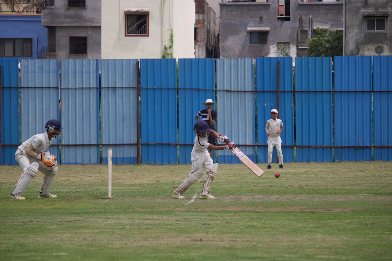 Action shot of teenagers playing cricket on a grassy field in Gahunje, India.